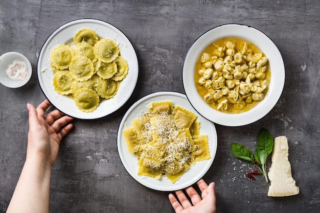 Foto vários tipos de ravióli italiano cozido em pratos sobre a mesa caseira servindo com queijo parmesão e mãos femininas