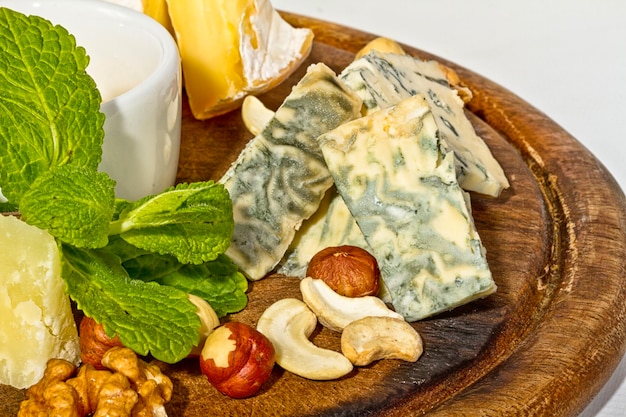 Varios tipos de queso con nueces de miel y uvas en un plato aislado en blanco