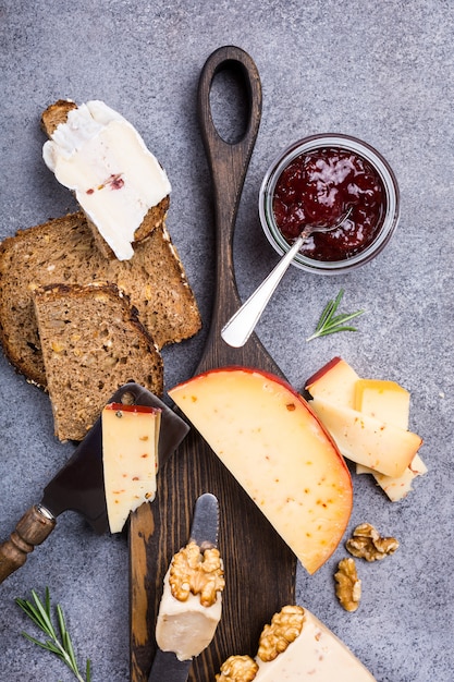 Varios tipos de queso con pan integral, mermelada de fresa y nueces.