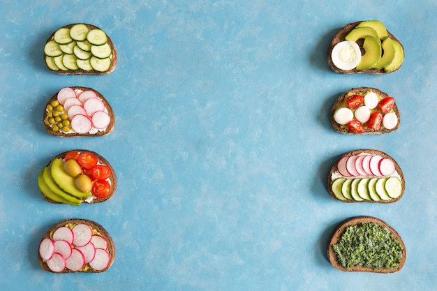 Varios tipos de sándwiches caseros con verduras planas yacían sobre fondo azul concreto con espacio de copia