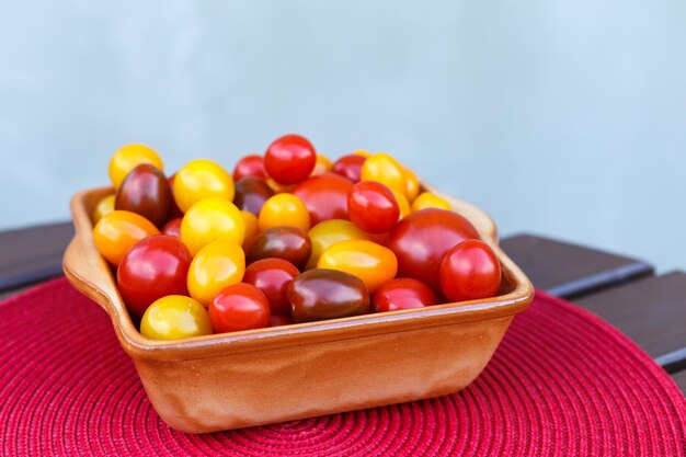 Vários tomates cereja coloridos em uma tigela de cerâmica Alimentação saudável ou conceito vegetariano