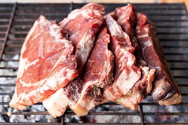 Varios trozos de carne cruda al lado de una parrilla caliente