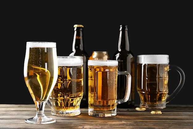Vários utensílios de vidro com cerveja em mesa de madeira contra fundo preto