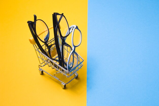 Varios vasos diferentes en un pequeño carrito de la compra sobre una superficie colorida