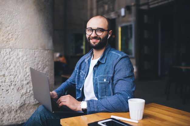 Varón alegre que usa la computadora portátil en café