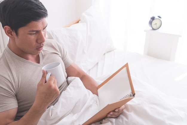 El varón asiático está estudiando y bebe café en la cama de la mañana