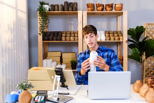 Varón caucásico vende productos de jarrón en línea con transmisión en vivo en casa Joven hombre atractivo usa un teléfono inteligente que muestra productos al cliente y presenta detalles Compra remota y concepto de compra de compras