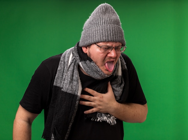 Varón enfermo de mediana edad con gorro de invierno y bufanda aislado en la pared verde