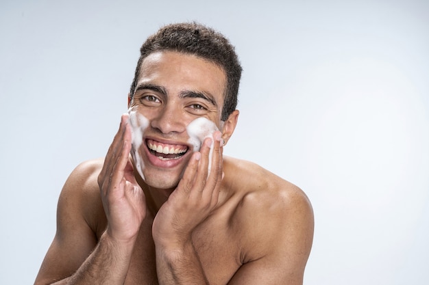 Varón joven alegre lavándose la cara con espuma limpiadora