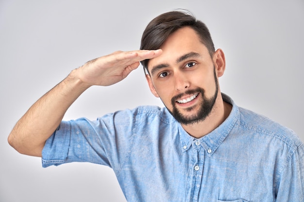 Varón joven caucásico en el futuro de miradas casuales mirando muy lejos con la mano sobre la cabeza aislado sobre fondo blanco Concepto de búsqueda