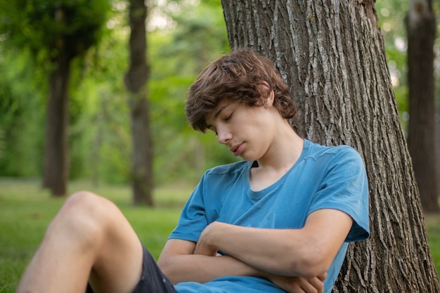 Varón joven durmiendo en el parque público sobre la hierba debajo del árbol