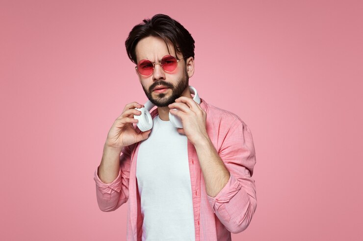 Varón joven con gafas de sol rojas sosteniendo en el cuello auriculares blancos