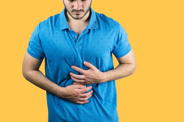 Varón joven que sostiene su vientre que sufre de dolor con un fondo amarillo