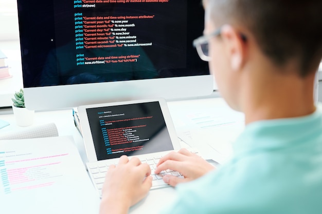 Varón joven sentado en el lugar de trabajo mientras presiona los botones del teclado de la computadora e ingresa datos