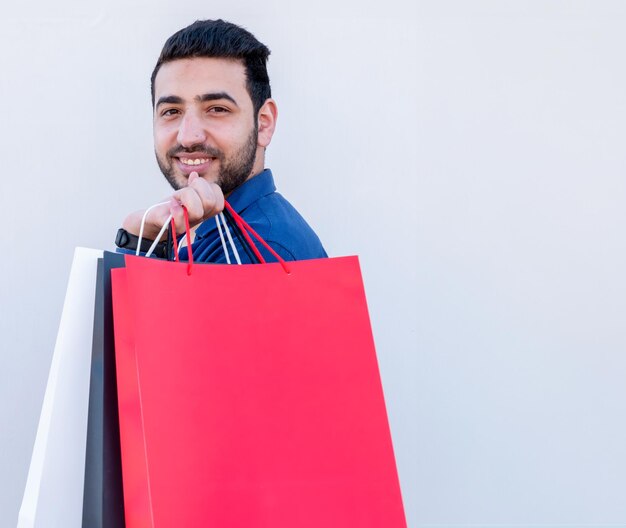 Varón joven sosteniendo bolsas de compras sobre fondo blanco aislado para promociones de viernes en blanco y negro con cara alegre