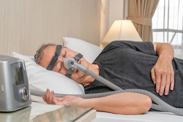 Foto varón de mediana edad con apnea del sueño usando máscara y casco de cpap mientras duerme