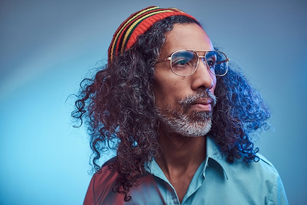 Varón rastafari africano con camisa azul y gorro. Retrato de estudio sobre un fondo azul.