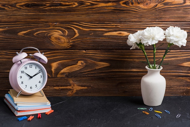 Foto vase; bunte büroklammer; wäscheklammer und wecker auf notebooks über dem schwarzen hintergrund gestapelt