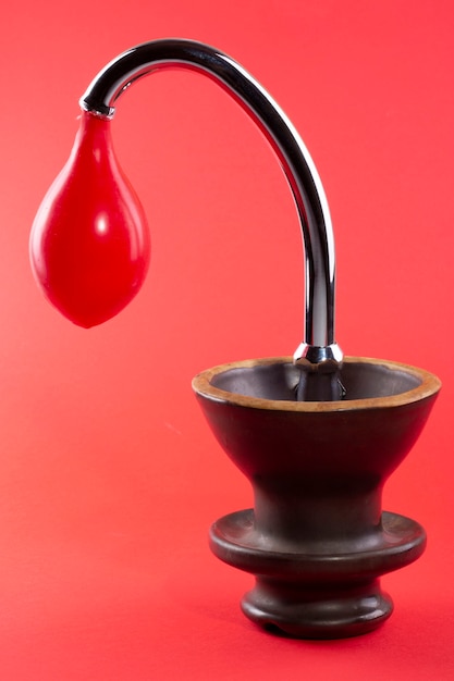 Vase mit einem Ballon in einem Wasserhahn auf rotem Grund