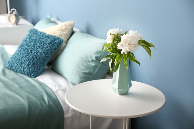 Vase mit schönen Blumen auf dem Tisch im Schlafzimmer