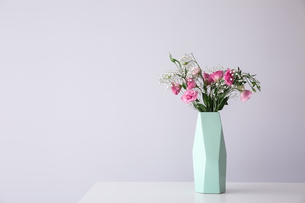 Vase mit schönen rosa Blumen auf Tisch vor hellem Hintergrund