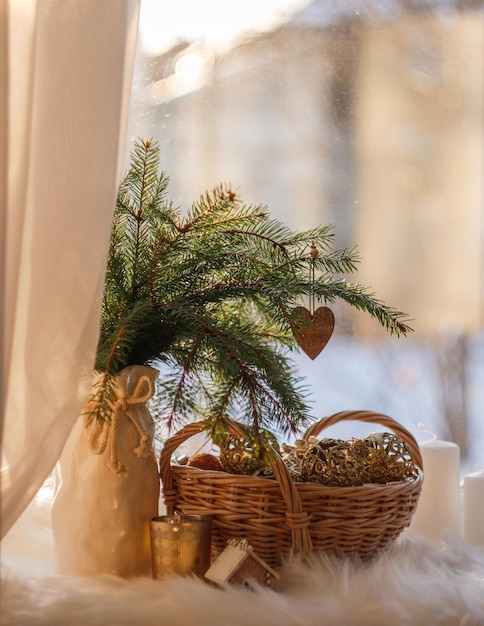 Vase mit Tannenzweigen und ein Korb mit Weihnachtsschmuck auf der Fensterbank