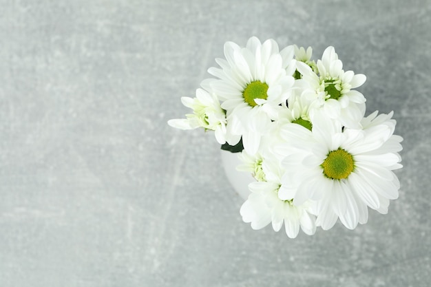 Vase mit weißen Chrysanthemen auf grauem strukturiertem Tisch.