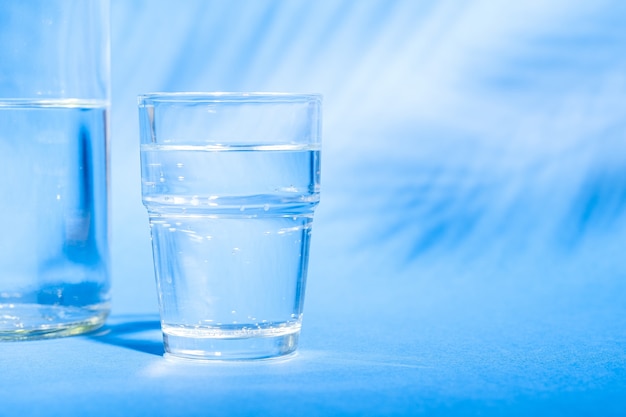 Vaso con agua cerca de la botella sobre fondo azul.