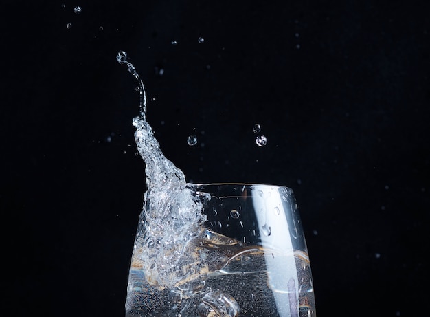 En un vaso de agua clara, las salpicaduras y las ondas se vierten sobre un fondo borroso