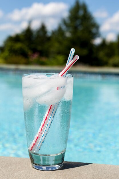 Vaso de agua con cubitos de hielo al lado de la piscina