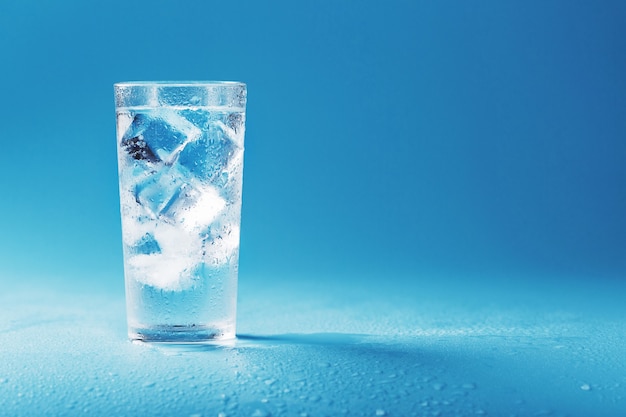 Vaso con agua y cubitos de hielo sobre un fondo azul. Concepto de rescate en un día caluroso y bochornoso. Espacio libre