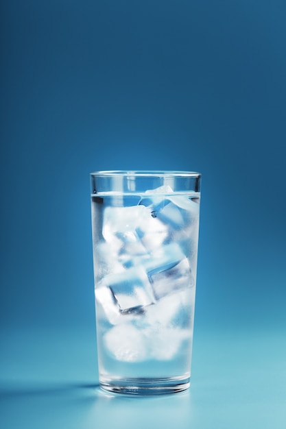 Vaso con agua y cubitos de hielo sobre un fondo azul.