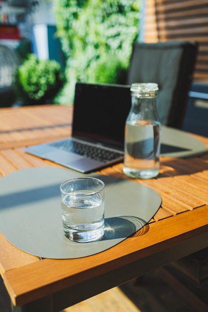 Un vaso de agua en el fondo de una computadora portátil en una terraza de verano Trabajar en un café Trabajo remoto en línea