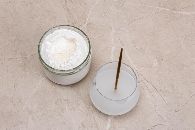 Vaso de agua y un frasco de bondad de colágeno sobre un fondo beige de mármol