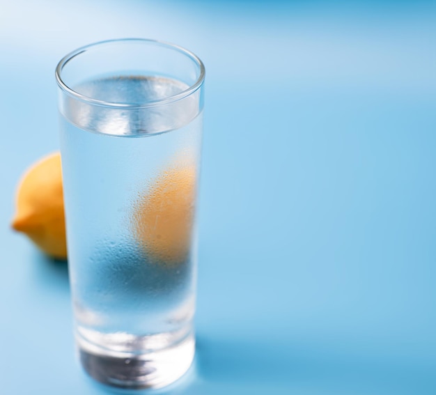 Vaso de agua fría pura con limón sobre un fondo azul.