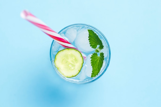 Vaso de agua fría y refrescante con hielo, menta y pepino sobre un fondo azul. Cubo de hielo. Concepto de verano caluroso, alcohol, bebida refrescante, calmar la sed, bar. Vista plana, vista superior