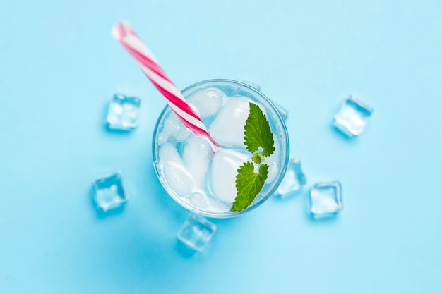 Vaso de agua fría y refrescante con hielo y menta sobre un fondo azul. Cubo de hielo. Concepto de verano caluroso, alcohol, bebida refrescante, calmar la sed, bar. Vista plana, vista superior