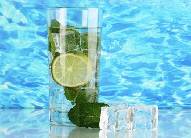 Vaso de agua con hielo, menta y lima sobre fondo marino