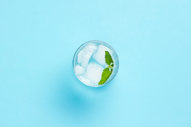 Vaso de agua con hielo y menta sobre un fondo azul. Concepto de verano caluroso, alcohol, bebida refrescante, calmar la sed, bar. Vista plana, vista superior