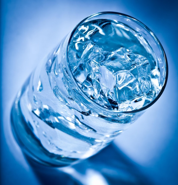 Vaso de agua con hielo sobre un fondo azul oscuro