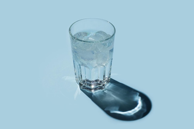 Vaso de agua con hielo sobre fondo azul.