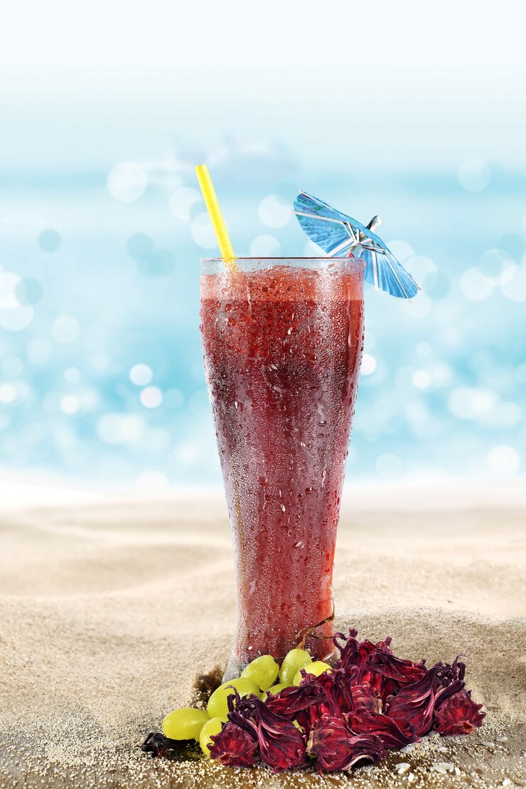 Vaso con agua de Jamaica y uvas en la arena de la playa
