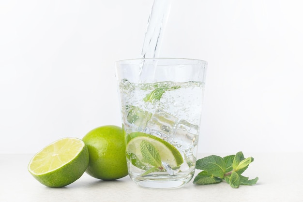 vaso de agua con lima helada y menta sobre un fondo gris claro