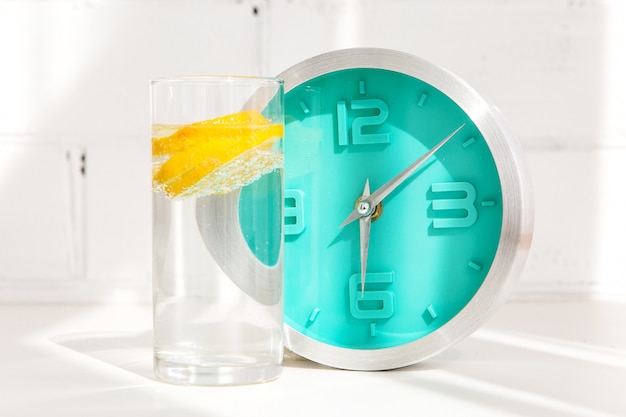 Vaso de agua con limón y reloj.