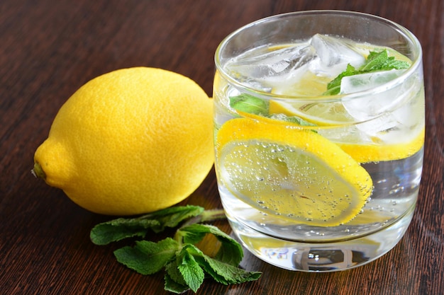 Un vaso de agua de limón con rodajas de limón, cubitos de hielo y menta aislado