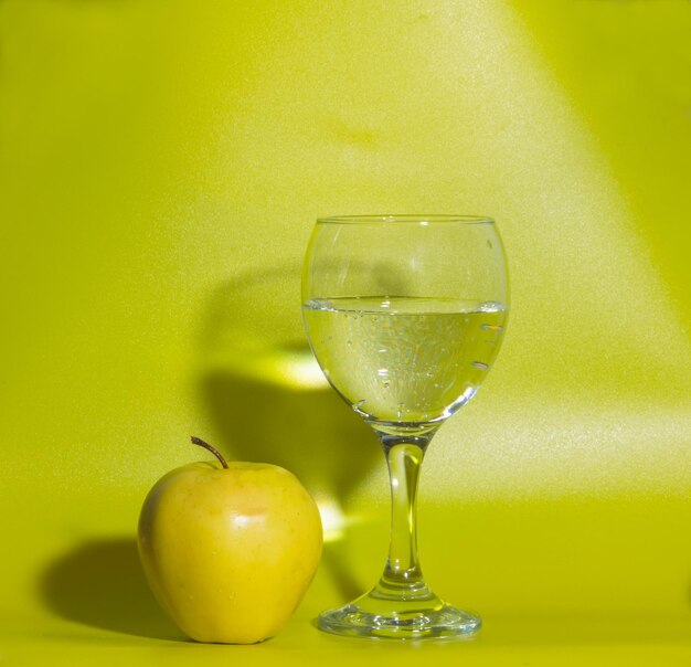 Un vaso de agua y una manzana amarilla sobre un fondo verde.