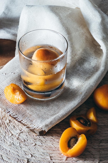 Vaso de agua con melocotones sobre mantel y tablero de madera