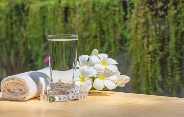 Foto vaso de agua en una mesa de madera con flor blanca y pañuelo en el fondo de la naturaleza.