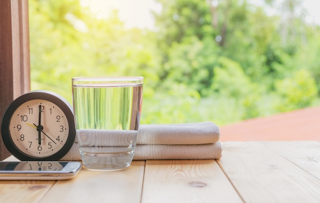 vaso de agua en una mesa de madera con reloj y pañuelo en el fondo de la naturaleza.