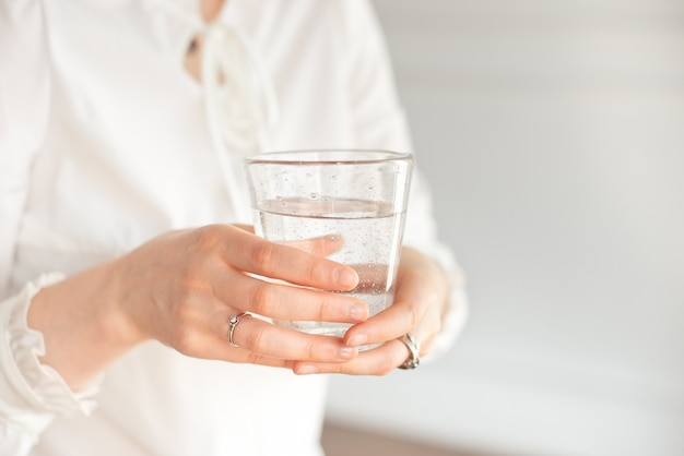 Vaso de agua mineral limpia en manos de mujer.